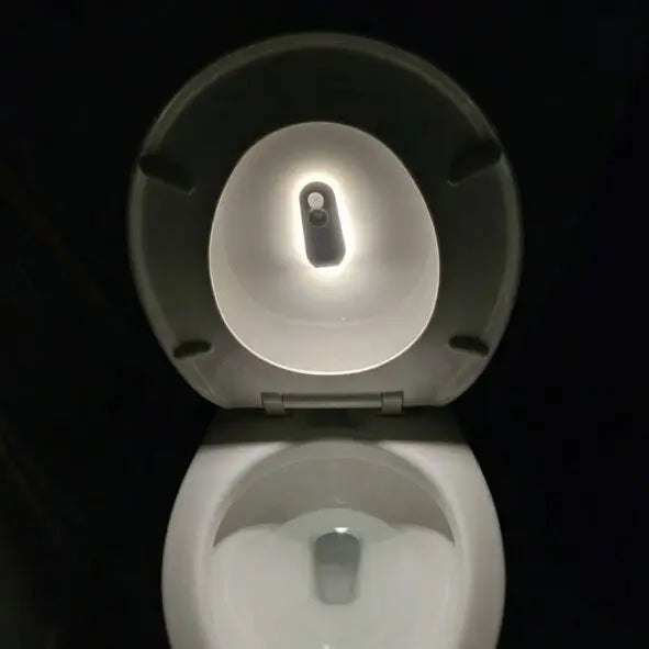 Smart toilet seat with motion-activated night light illuminating bowl in dark bathroom