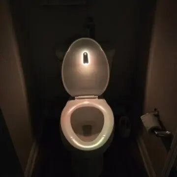 Smart toilet with illuminated seat and lid in dim bathroom, featuring motion-activated night light